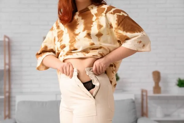 Image of woman trying to do her trousers up after pregnancy weight gain Cardonald